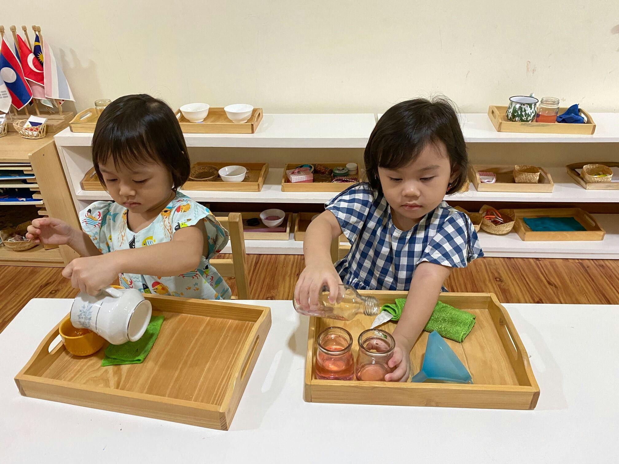dua murid belajar untuk menuang air menggunakan peralatan Montessori