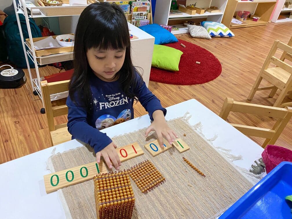 A child learning the decimal system with golden bead materials and number cards