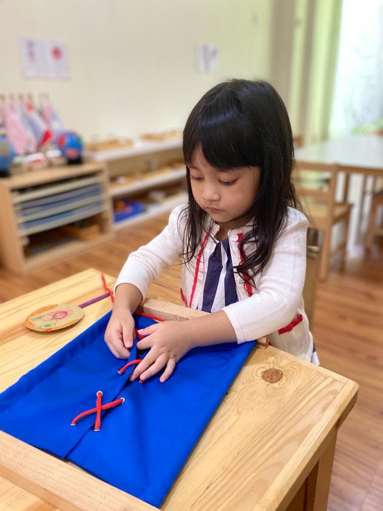 Seorang anak berlatih menyulam tali pada dressing frame Montessori