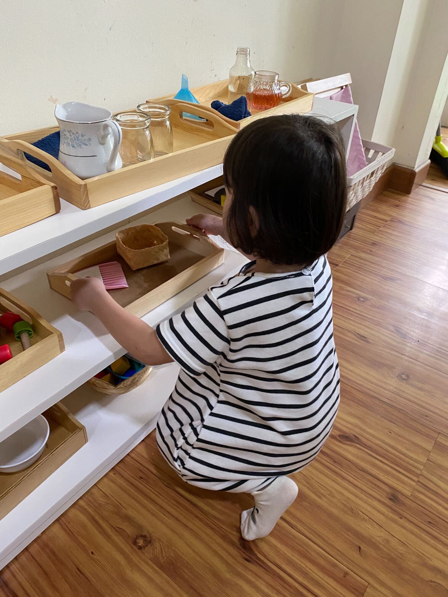 A child choosing a practical life activity from a low Montessori shelf