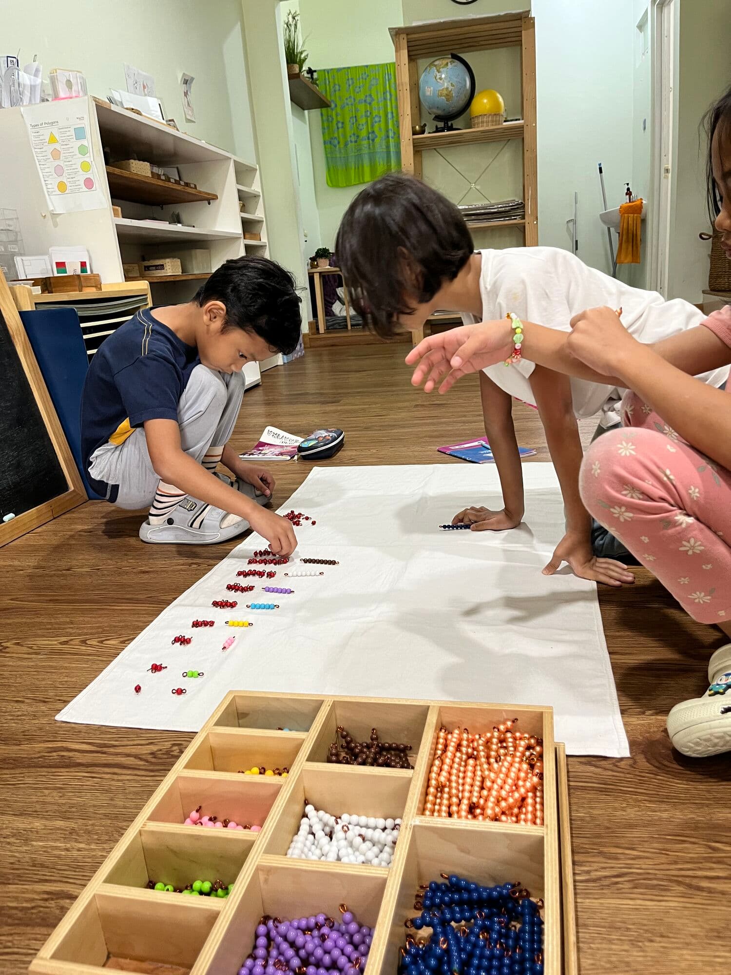 Students arranging colorful bead chains on a floor mat during a math activity