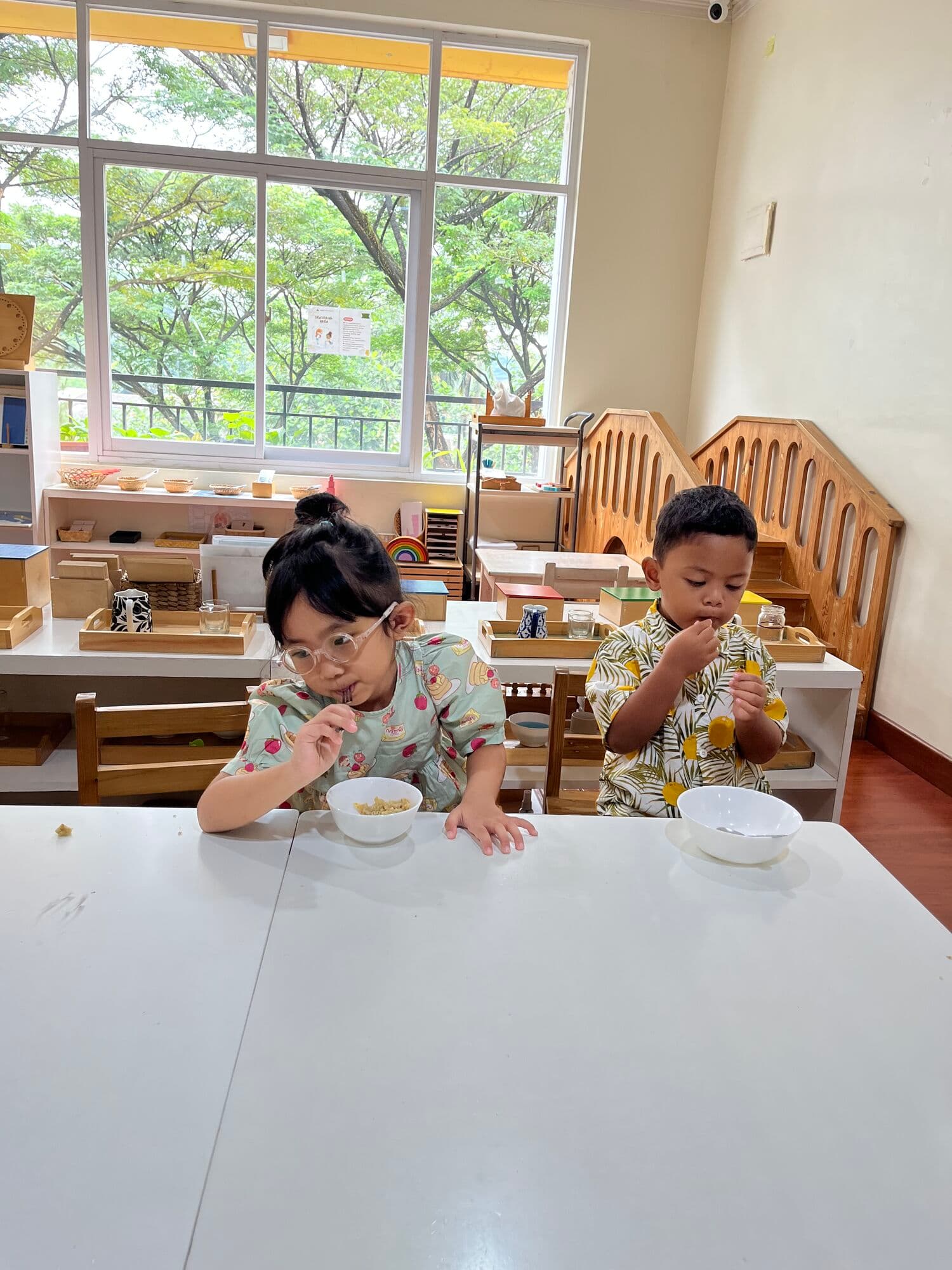 Dua anak makan camilan secara mandiri di meja kelas